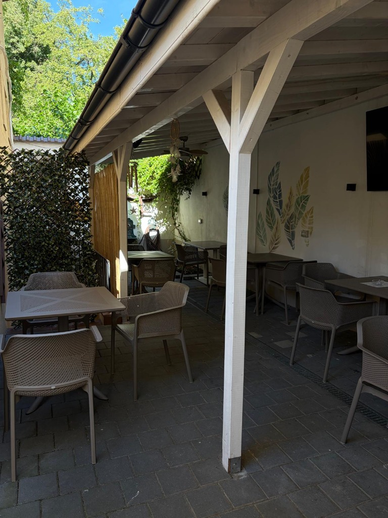 Bistro Papas terrace in daylight — white pergola, green trees, leaf murals